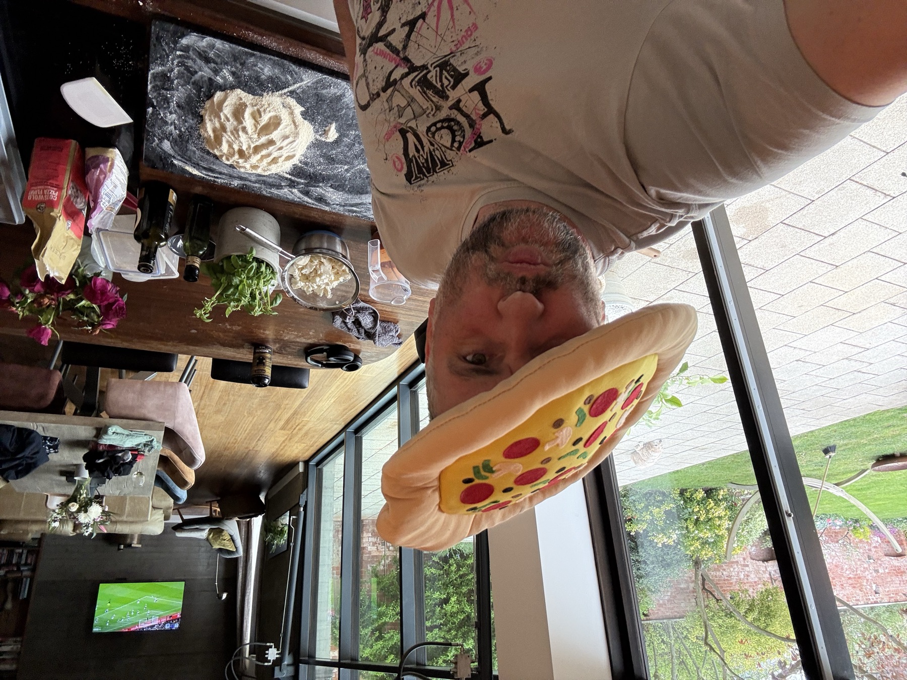 Gwyn in a pizza hat, making pizza, the garden through the glass